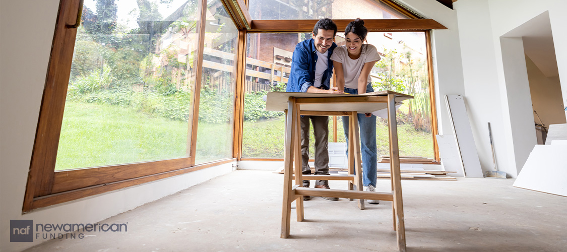 A smiling couple looking at blueprints in their under-construction home