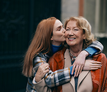 Dekle, ki je srečalo babico na sprehodu v mestu, jo objema in poljublja na lice.