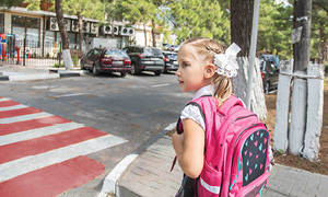 Deklica na prehodu za pešce čaka na varen trenutek za prečkanje