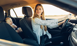 Mlada ženska za volanom avtomobila v poletnih mesecih uporablja klimo, da je njeni družini med vožnjo udobno.