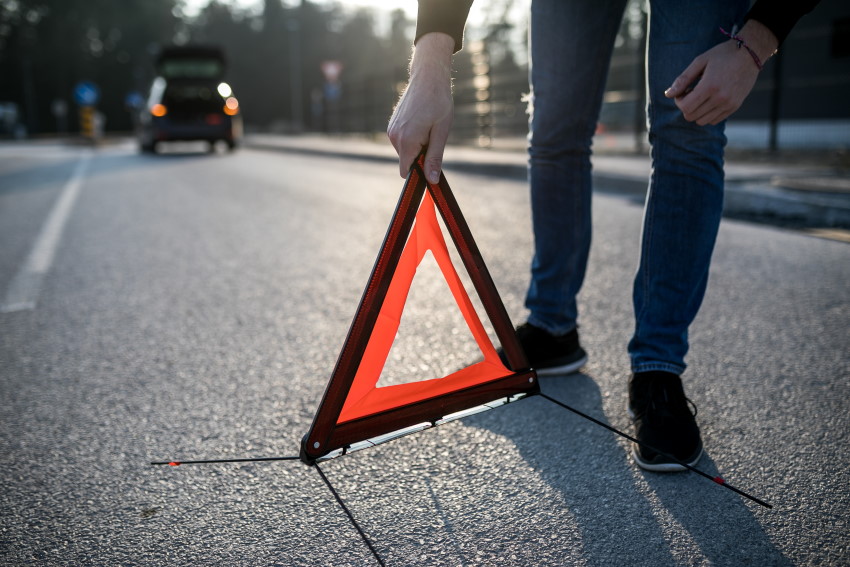 Voznik zaradi prometne nesreče postavlja varnostni trikotnik kot opozorilo drugim voznikom.
