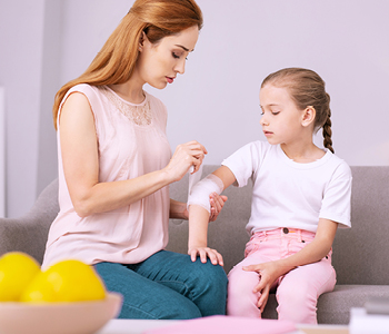 Mama hčerki v apartmaju nudi prvo pomoč po tem, ko si je odrgnila komolec.