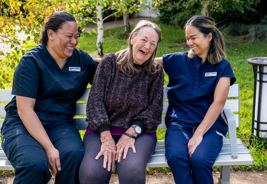 Three ladies are talking and laughing on a bench outside. Two are nurses from Benjamin Short Grove and they are talking to a elderly woman who is a resident.