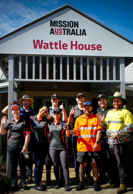 A group of males and females stand outside Wattle House, a Mission Australia service.