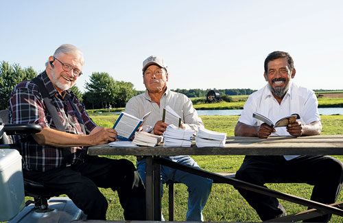 xDeacon Tony Hogervorst (left) shares CIS booklets with Juan Mosqueda Zavala (center) and Ad&aacute;n De Paz Magarino, migrant workers from Mexico whom Hogervorst employs on his farm in Watford, Ontario. A member of St. Isidore the Farmer Council 10141 in Watford, Deacon Hogervorst also makes CIS materials available to other migrant workers in the diocese.