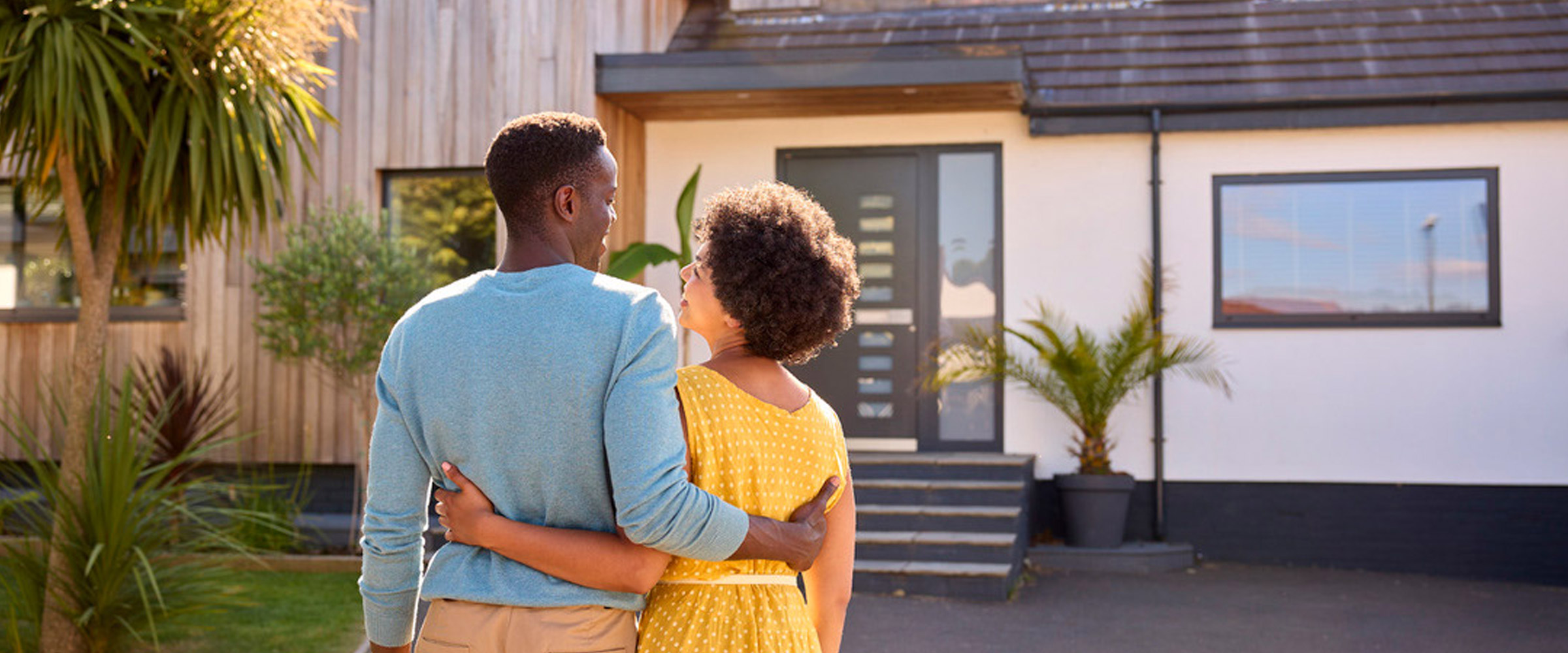 A couple facing holding each other and facing a home.