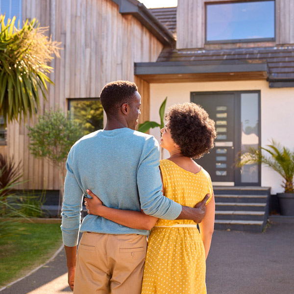 A couple facing holding each other and facing a home.
