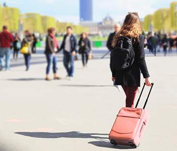 Dekle se v Parizu po ulicah sprehaja z nahrbtnikom in kovčkom.