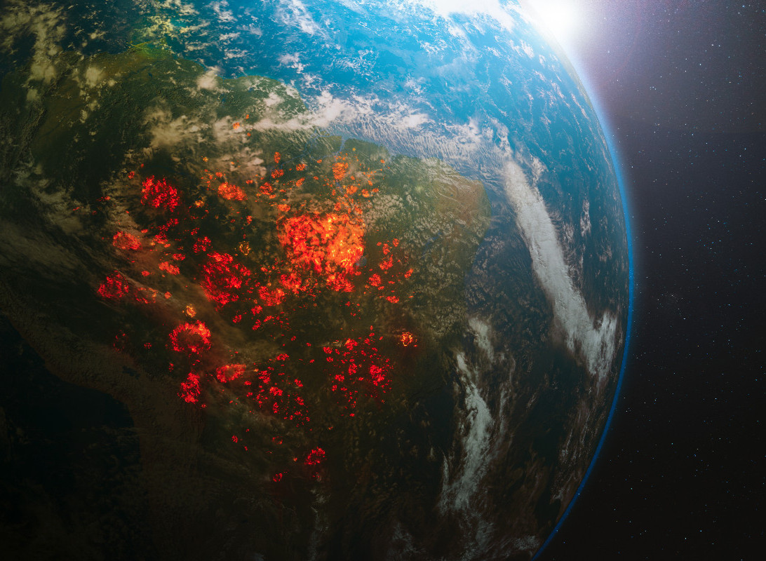 Satellite view of Earth showing a large, concentrated area of bright red and orange hot spots, likely representing wildfires, covering a major continental landmass, possibly South America's Amazon region, seen from space with the sun shining brightly on the horizon