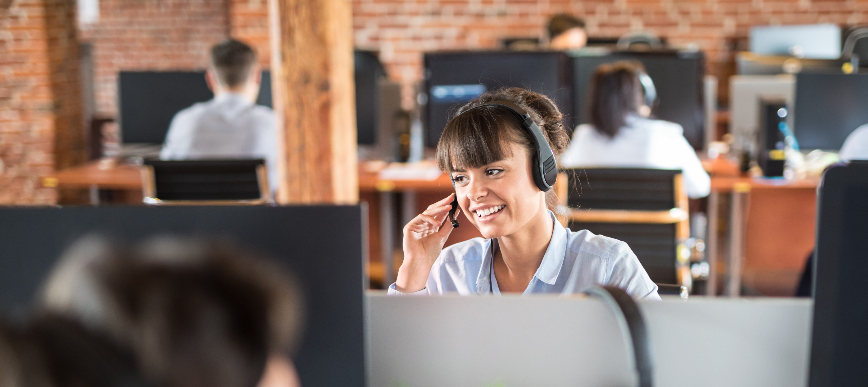 Smiling young woman with headset working in callcentre, surrounded by colleagues