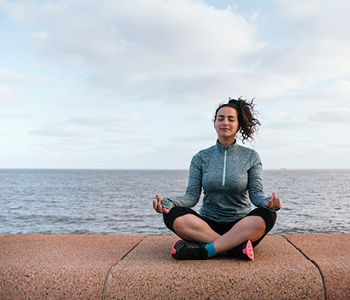 Mlada ženska meditira na nabrežju morja.