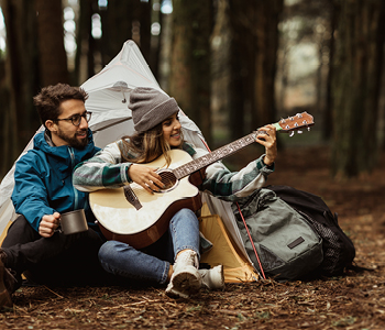 Mlad par na kampiranju v gozdu - dekle igra na kitaro.