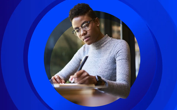 A head-and-shoulders image of a young person wearing glasses and a gray turtleneck, looking down and writing with a pen in a notebook or on paper, framed by concentric blue circles.