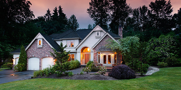 A nice brick and vinyl house with glowing lights on inside and a landscaped yard