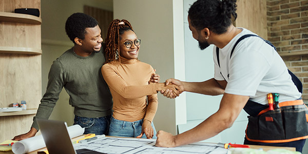 A smiling Black woman shakes hands with a Black man who is wearing a tool belt