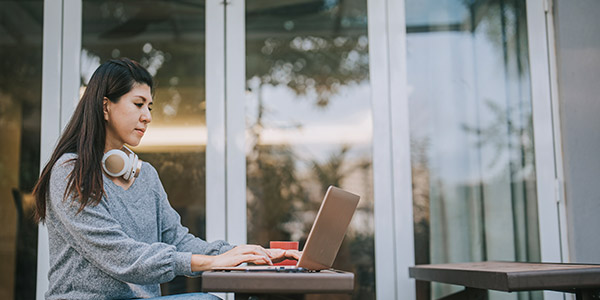 asian woman on a laptop with her headphone on her shoulders