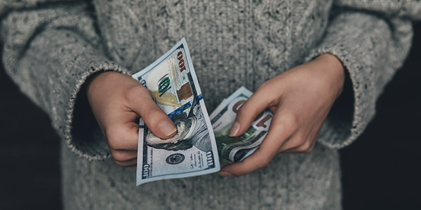 A person is holding several one-hundred dollar bills in their hands