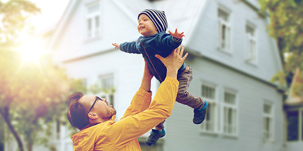 father playfully tossing his son up in front their house