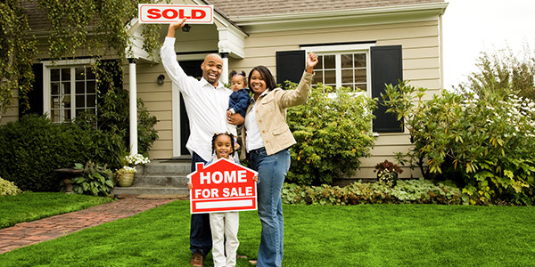 black family standing with a sold sign in front of their new home