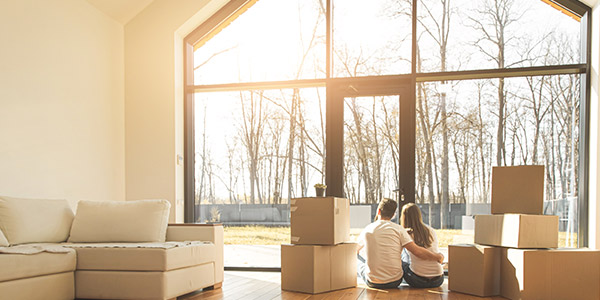 couple sitting on the floor and looking into yard of their new house surrounded by moving boxes