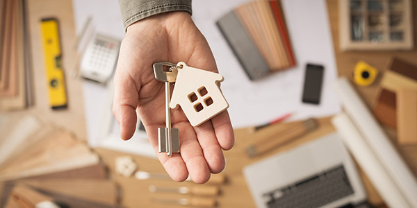 A hand holding a key ring with a key and a small model of a house