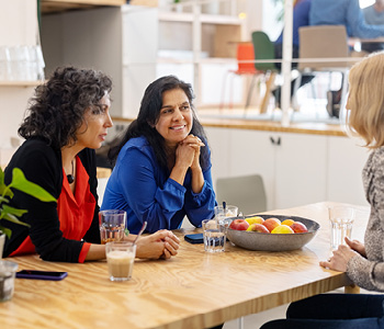 Tri ženske v pisarni trajnostno uživajo kavo iz klasičnih skodelic, skuhano v pisarniški kuhinji.