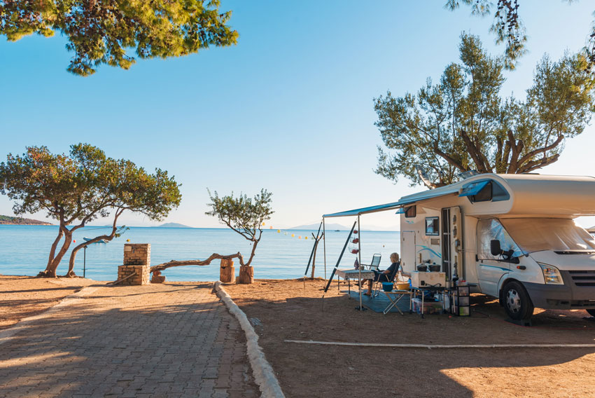 Avtodom z razprto tendo, parkiran na obali ob sončnem zahodu.