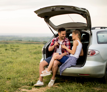 Mlad par sedi v prtljažniku avtomobila sredi polja - privoščila sta si samotni piknik na potovanju