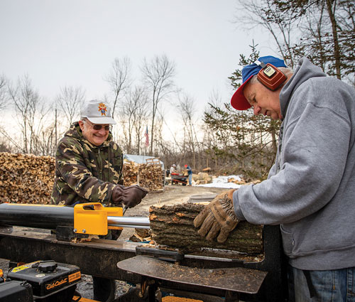 Two men outdoors cutting wood with a table saw