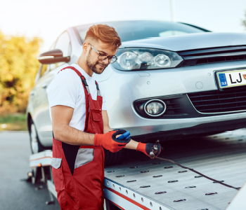 Avtovleka je prišla po okvarjan avto - mehanik avto nalaga na prikolico.