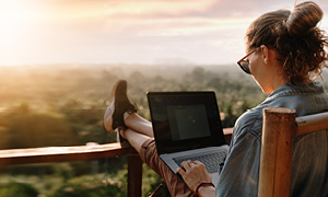 Dekle dela na računalniku na dopustu. Brez skrbi računalnik nosi s seboj na dopust, ker ga ščitijo močna gesla.