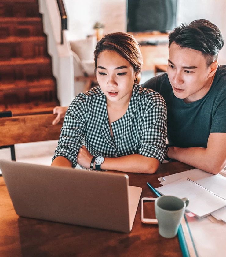 High angle view of couple sitting at dining room table with paperwork looking at laptop 