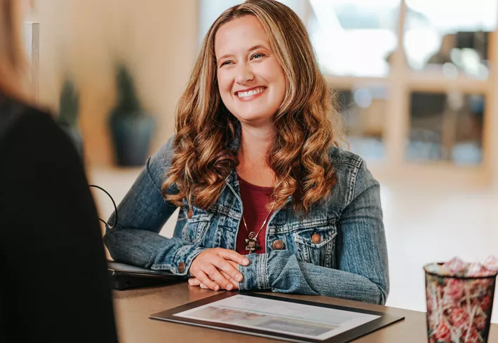 LMCU member at a LMCU front desk, smiling and interacting with another person, with documents and office items visible. 