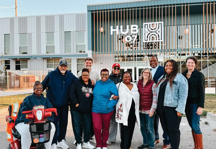 Group of people standing outdoors in front of a building with a ‘Hub 07’ sign, posing together for a photo. 