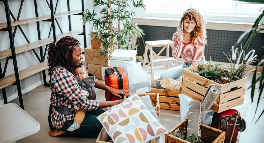 Couple sitting with baby while packing belongings in boxes to move. 