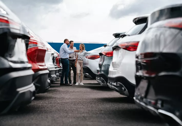 Car salesperson showing cars to a couple shopping at the dealership. 