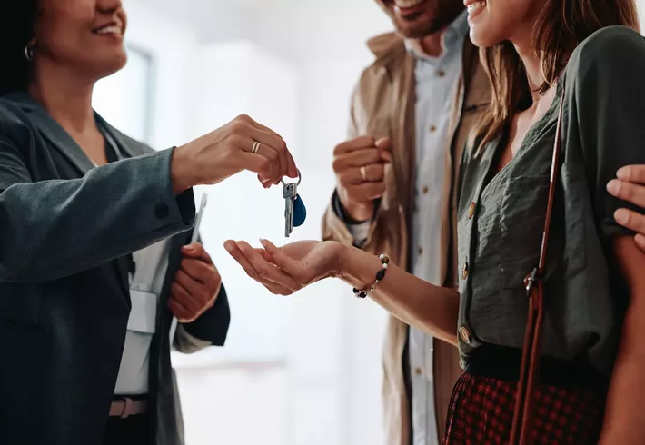 Woman in business attire handing a set of keys to a casual couple. 