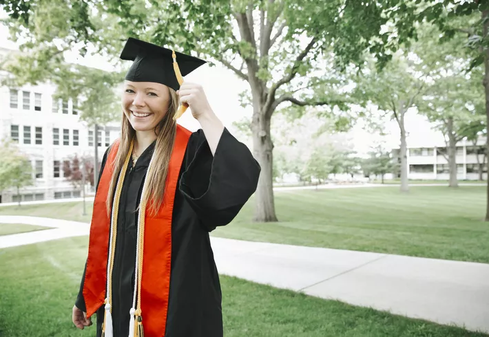 Female graduate in cap and gown with honor stole and chords. 