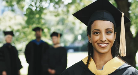 Female University graduate with yellow tassel on mortarboard. Other graduates in background. 